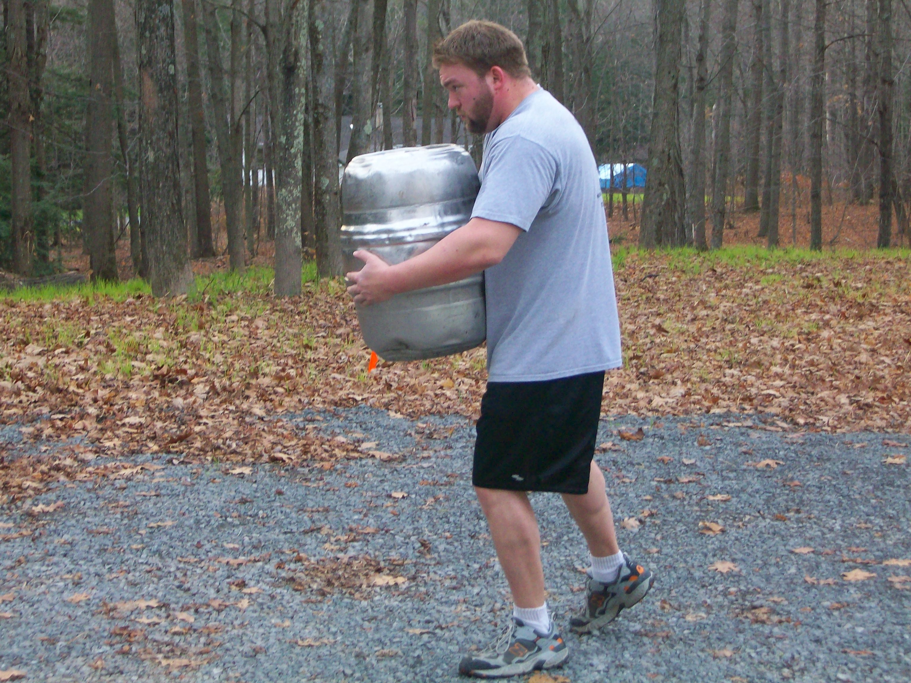 Man carrying keg and walking in woods.